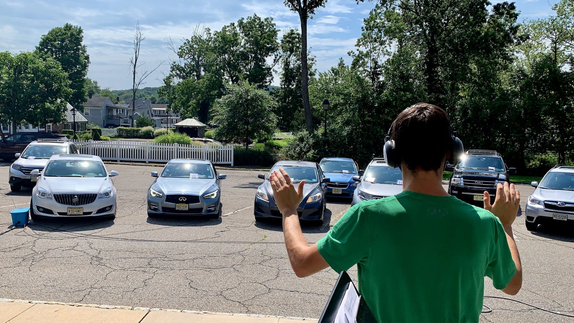 Man standing in front of cars with hands up conducting in a parking lot