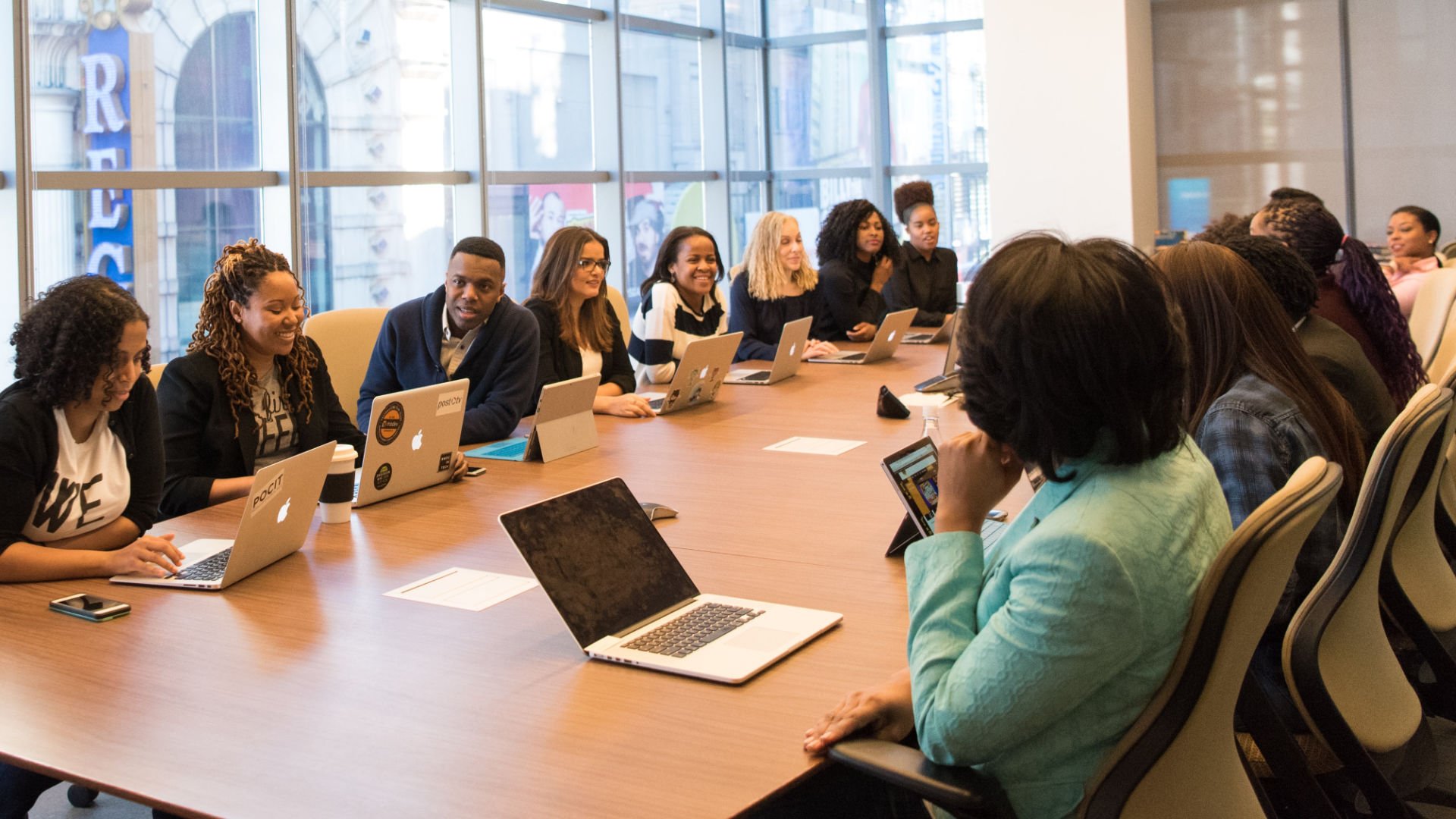 Fifteen young professionals seated at conference table smiling and collaborating 