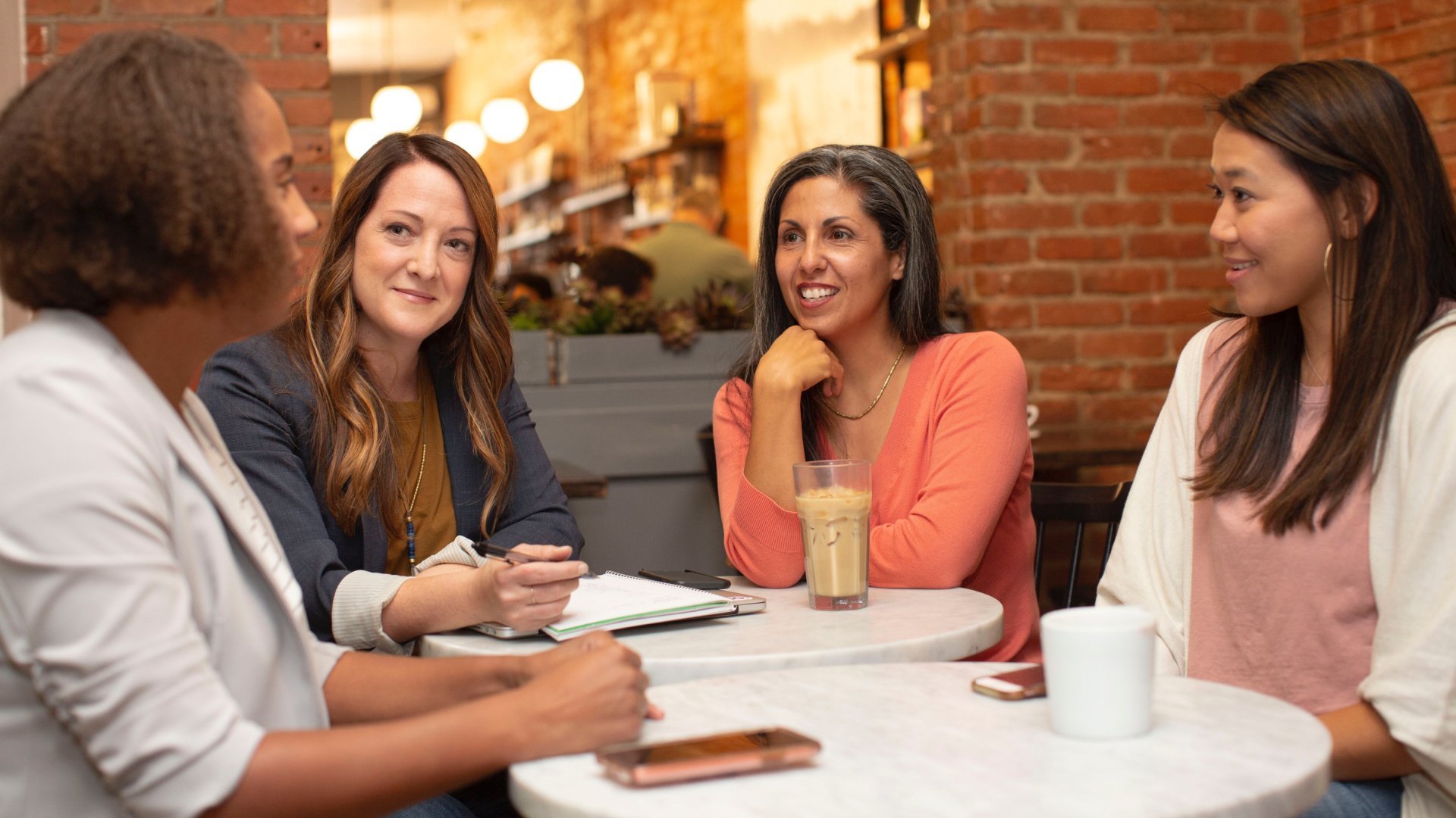 Four women sitting in coffee shop smiling in discussion