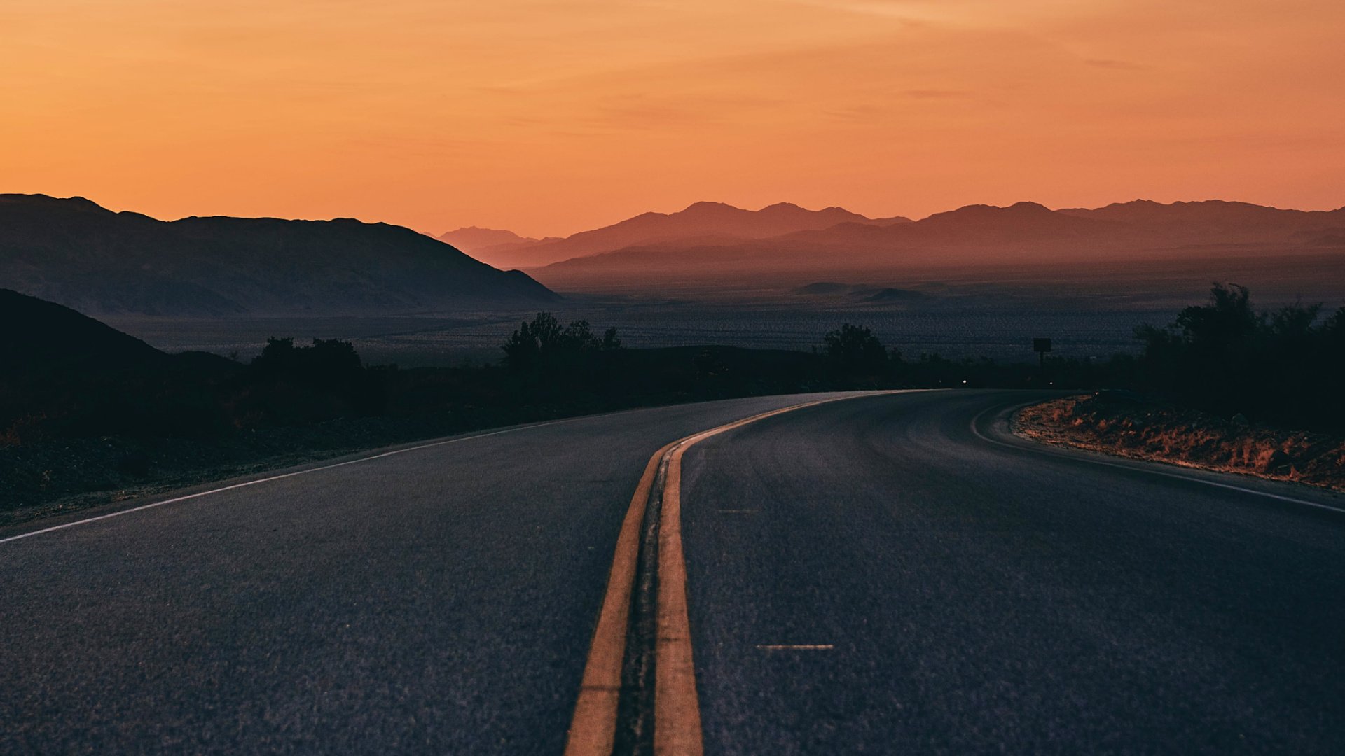 Close-up of highway curving to the right with sunset and mountains in the distance
