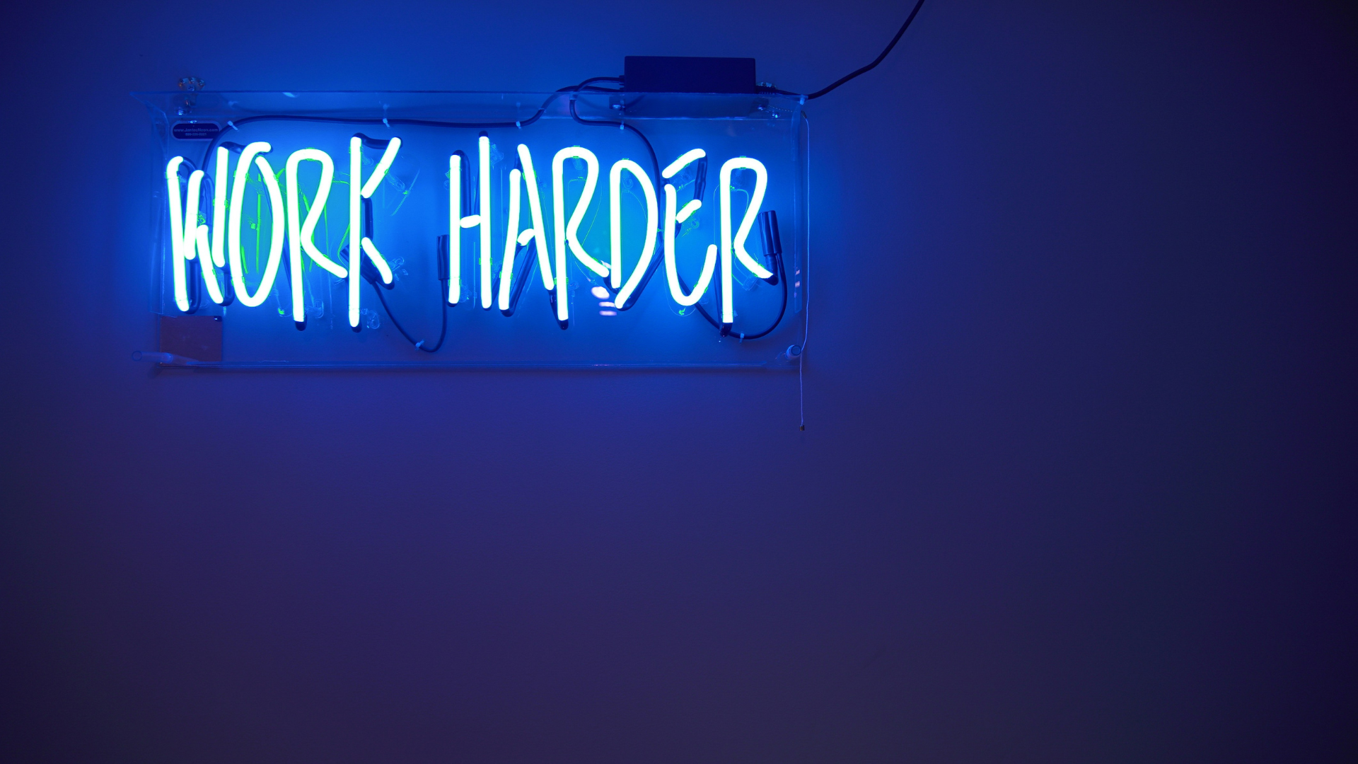 Blue neon sign with the words 'Work Harder' glowing in a dark room