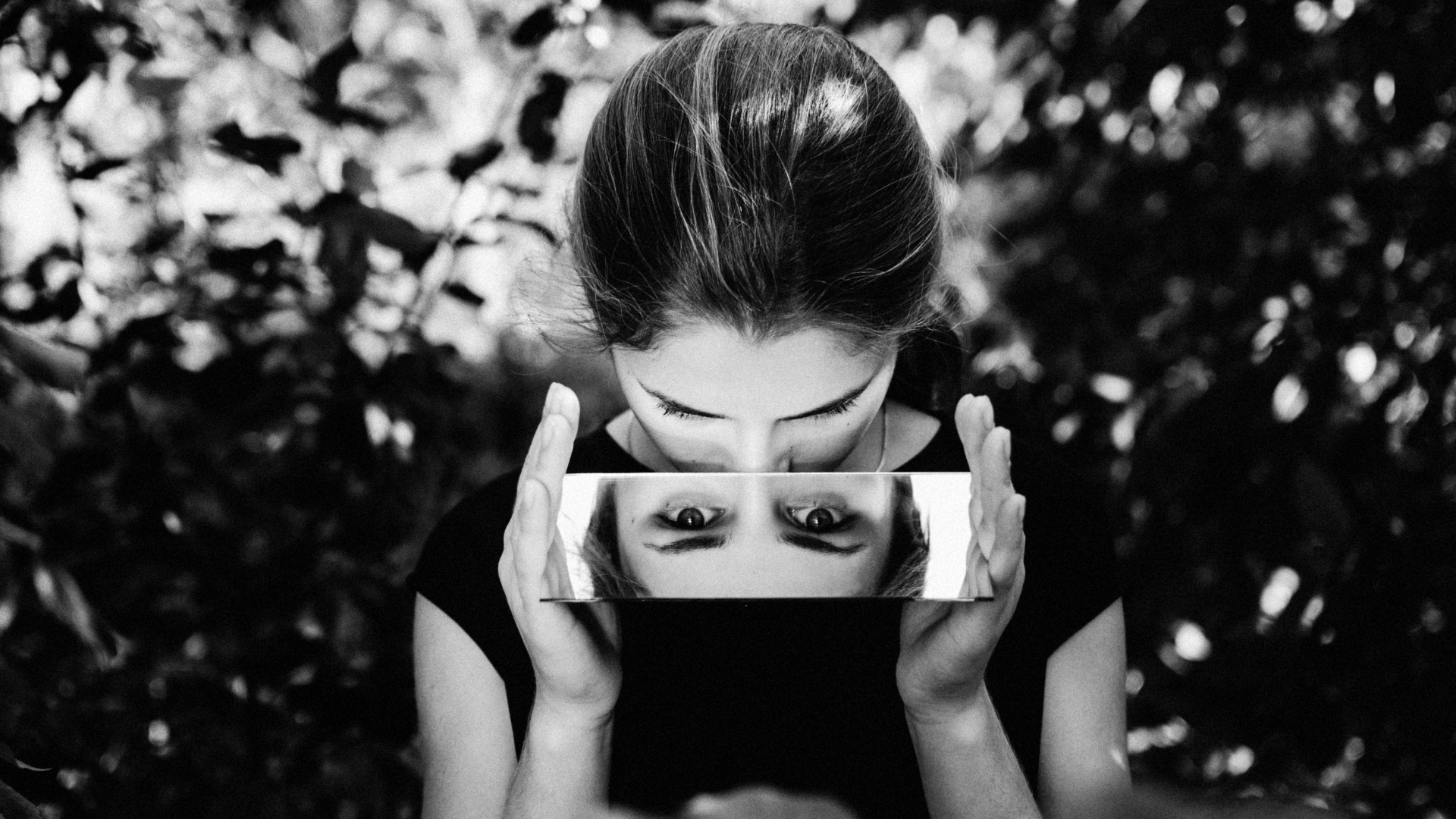Black and white photo of a woman's eyes reflecting back to the camera as she looks down at a the mirror she holds 