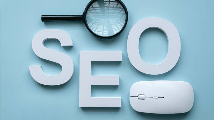 Stock photo with white 3D letters "SEO" on a light blue background and a computer mouse and magnifying glass