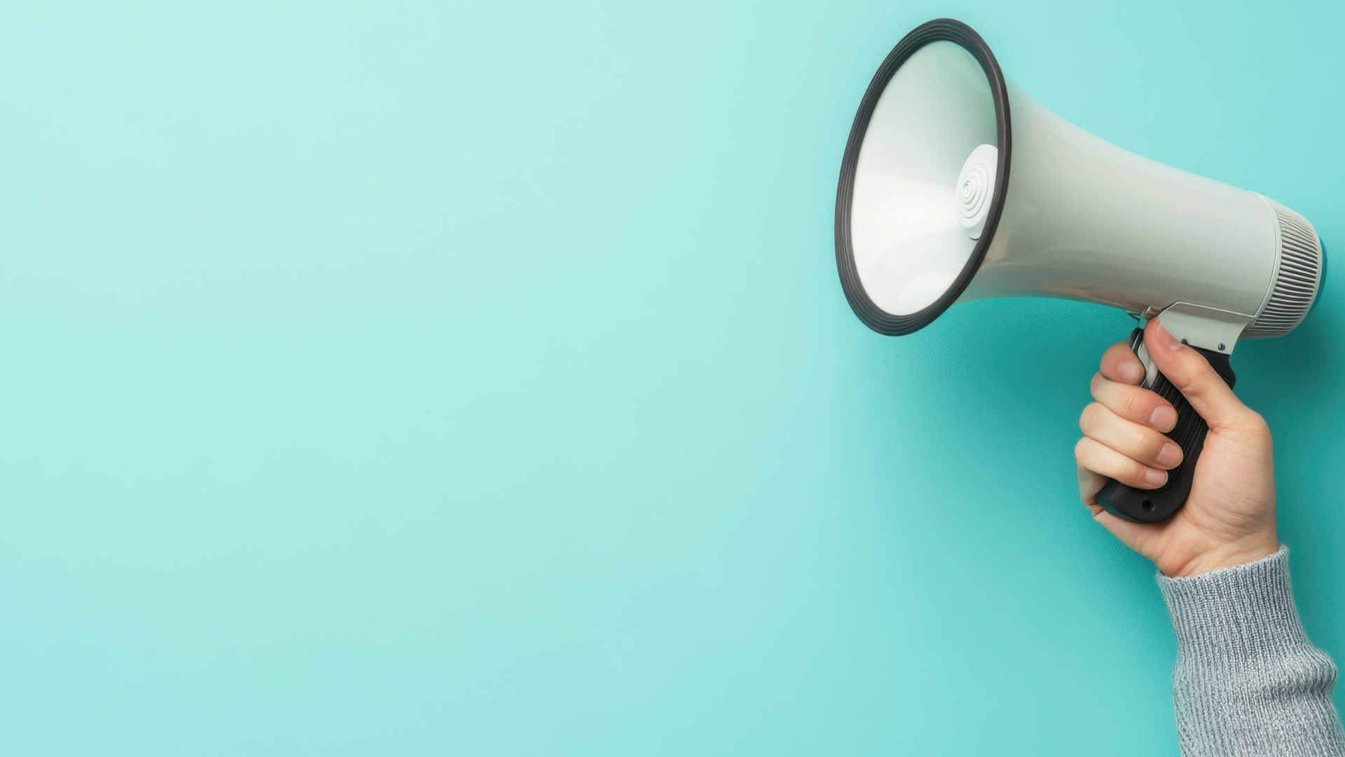 Photo of a hand holding up a megaphone against a turquoise background