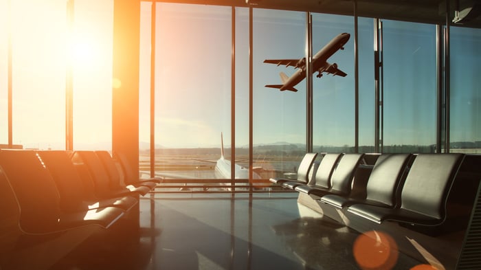 Photo of a plane taking off on a runway, viewed from the inside of an airport terminal