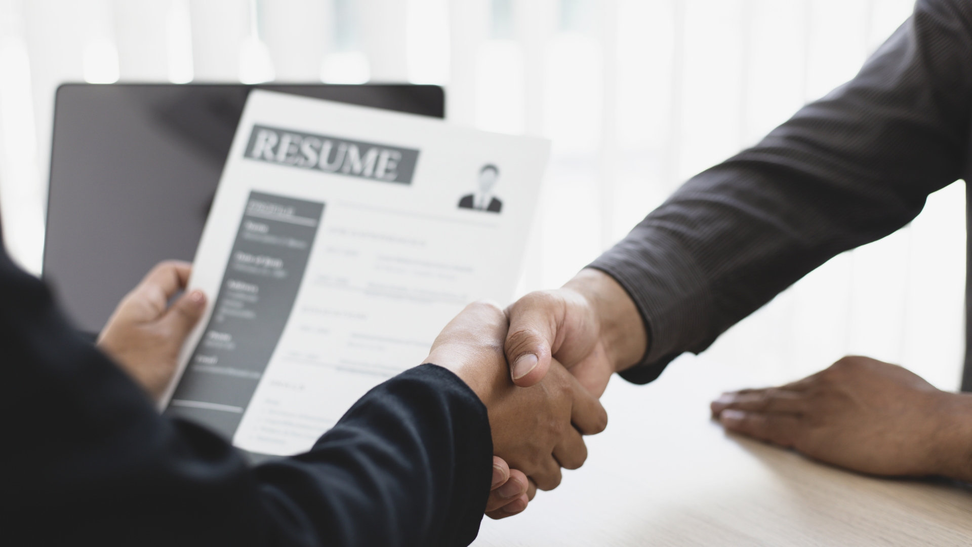 Closely cropped photo of two business people shaking hands as one holds the other's resume
