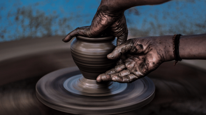 A close shot of a person's messy, clay-covered hands molding a curved vase as it spins on a pottery wheel