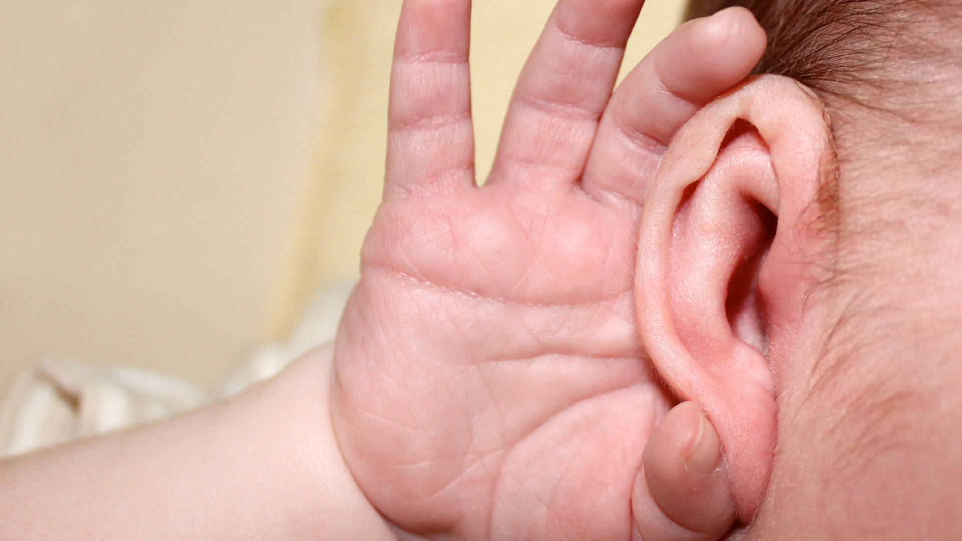 A tightly-cropped photo of a baby's hand cupped around its ear