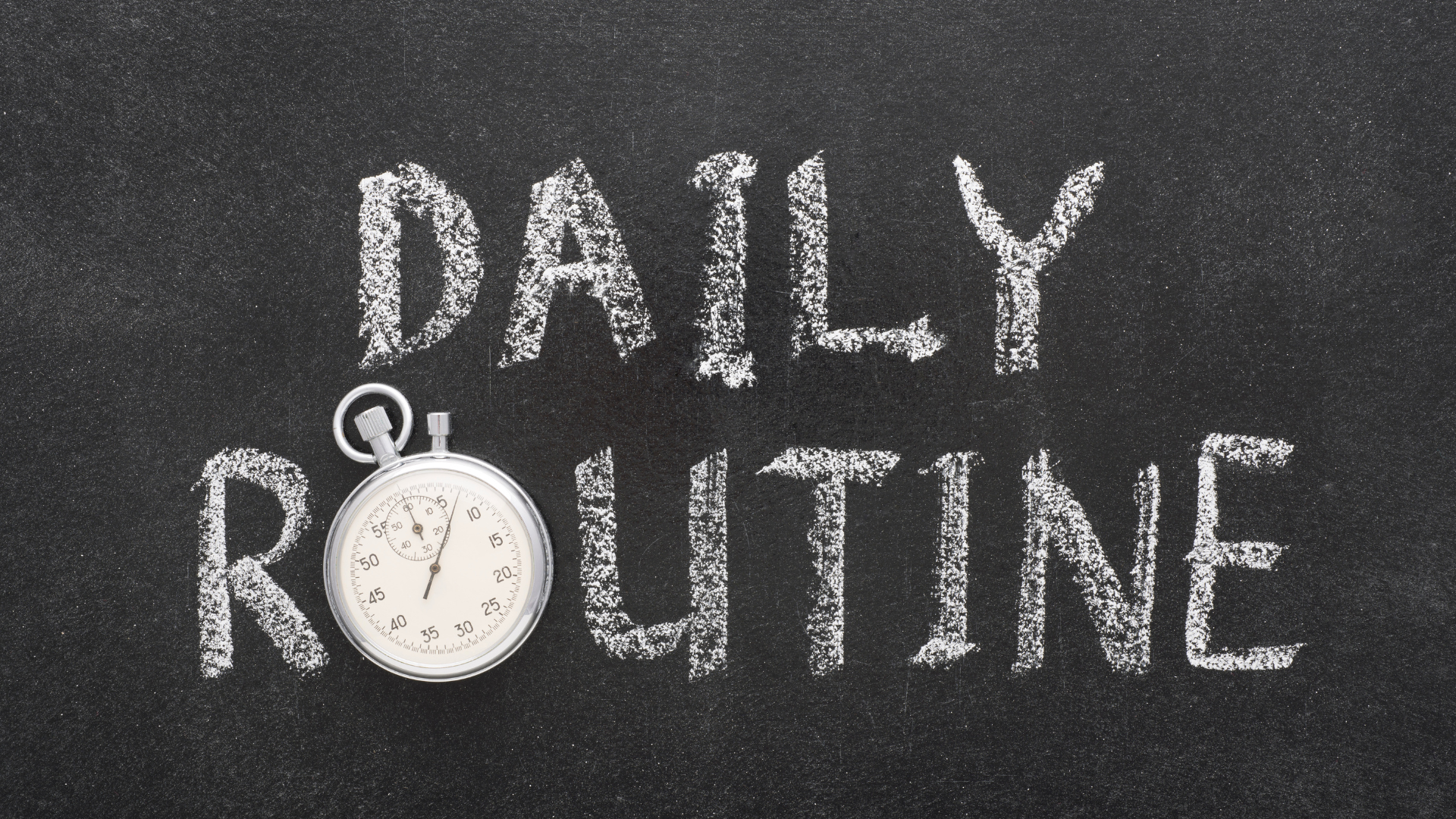 A photo illustration of a black chalkboard with the words "Daily Routine" written on it in white chalk. A stop watch is used in place of the "O" in routine.