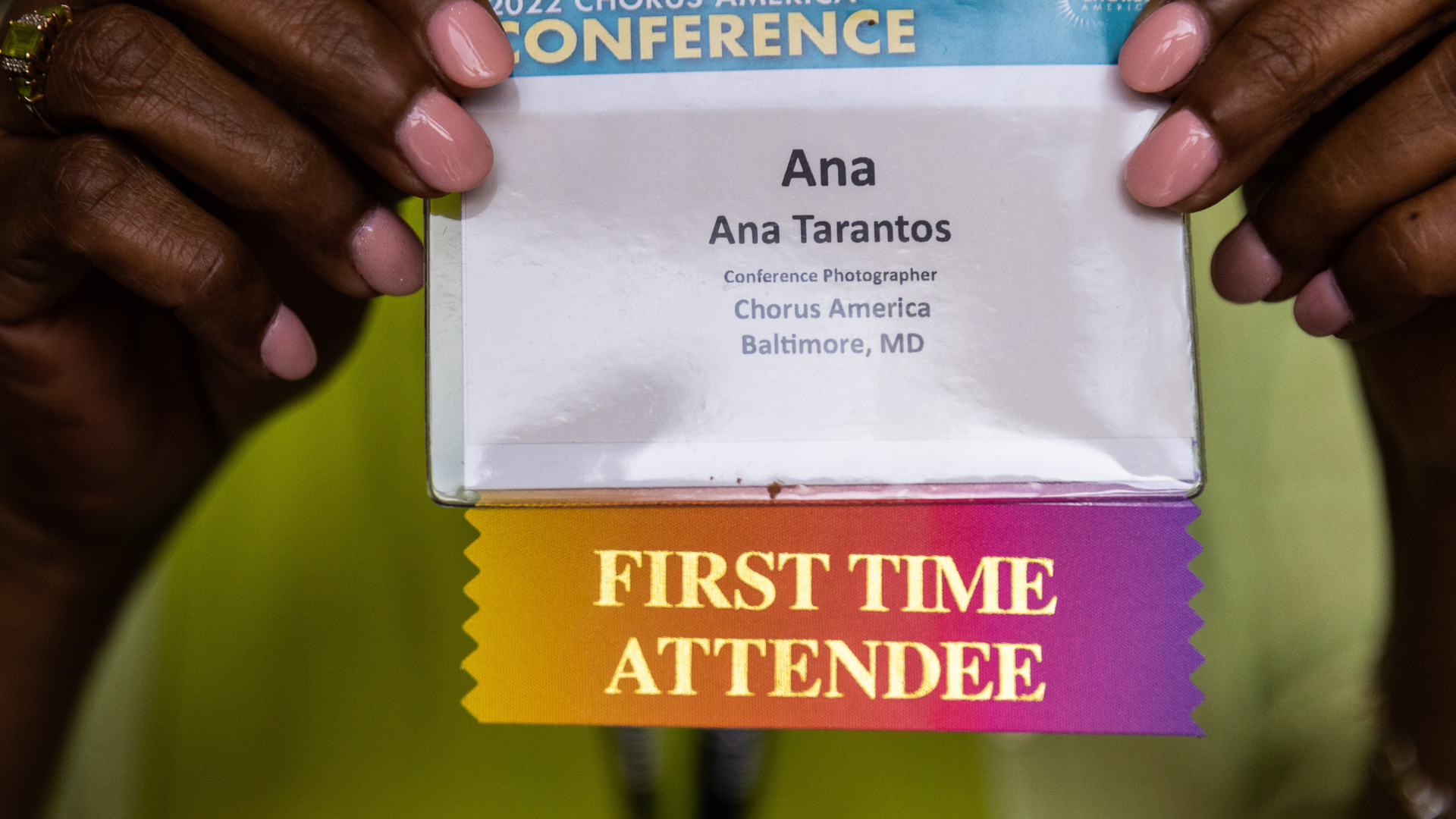 Close up photo of hands holding a rainbow colored name tag with "First Time Conference Attendee" embossed in gold