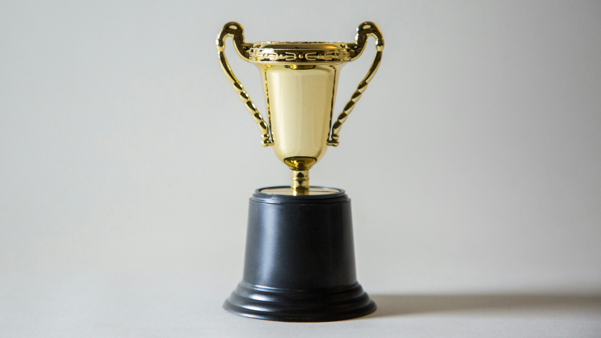 A shiny gold trophy stands against a blank white backdrop