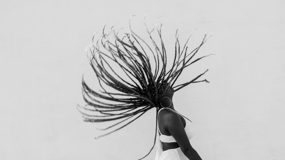 Black woman in white dress flipping their long braided hair backwards in black and white photography