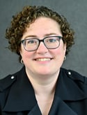 Woman with short curly hair wearing black frame glasses smiles at the camera - Christie McKinney Headshot