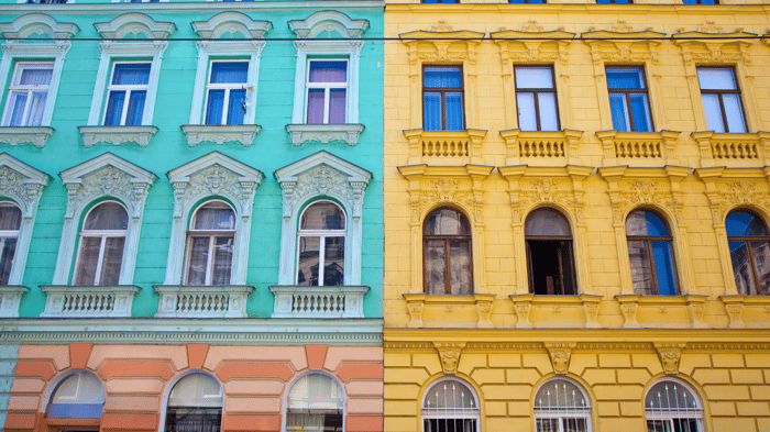 Side-by-side view of two ornate European-style buildings, one painted turquoise with peach trim and the other painted yellow with detailed architectural accents.