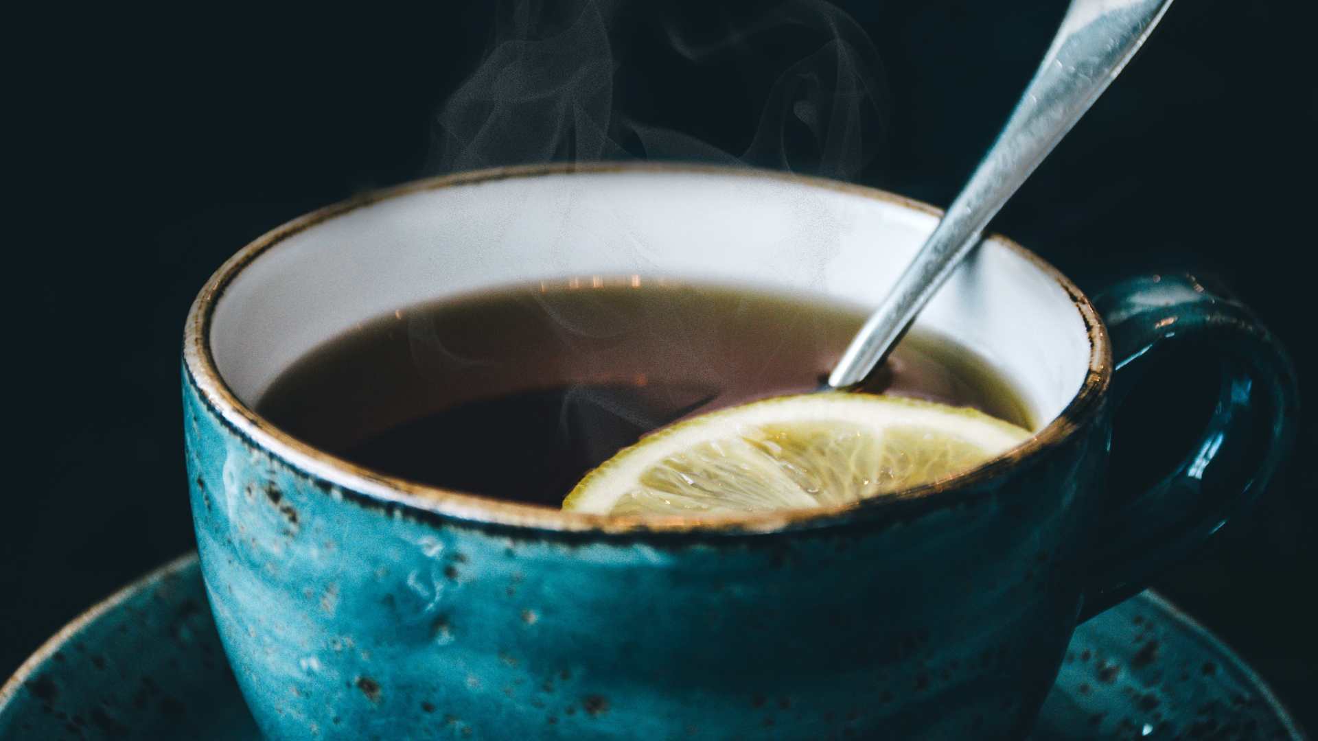 Close up photo of a hot cup of steaming tea with a spoon and lemon wedge floating in the liquid