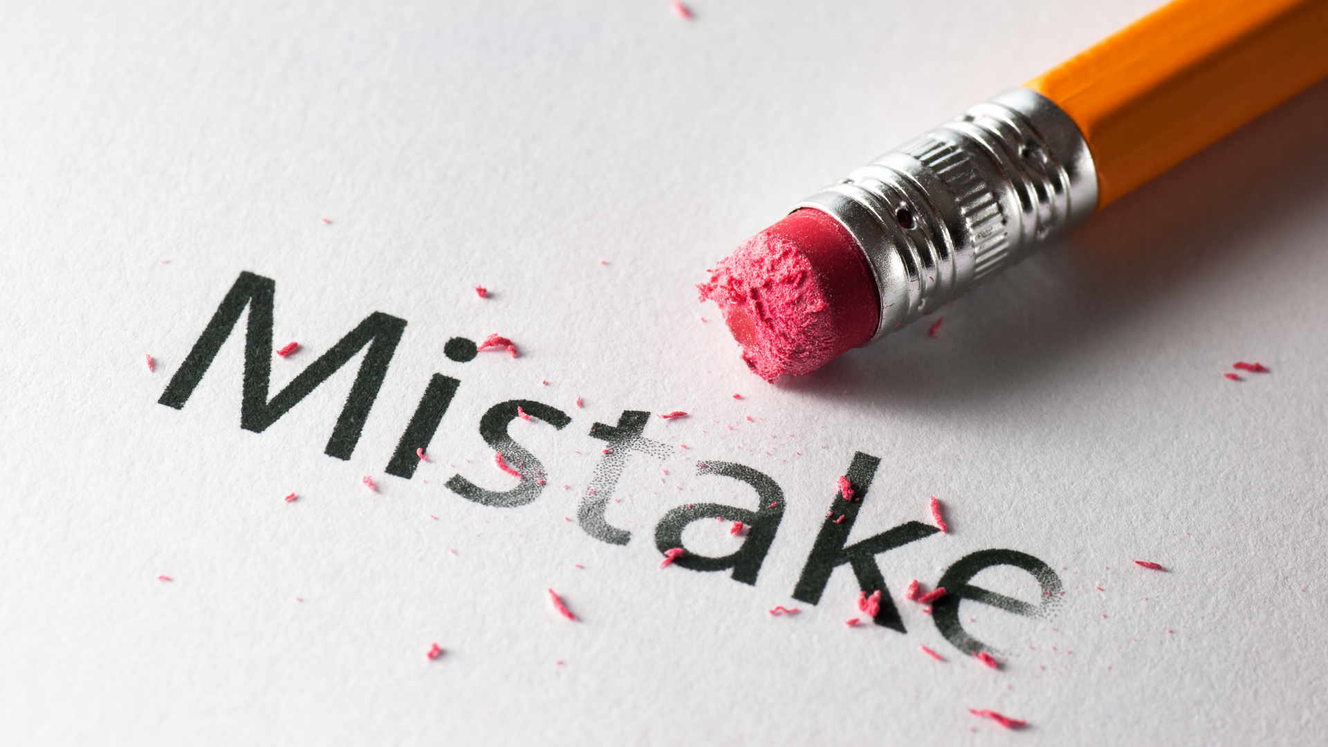 Close-up of a pencil erasing part of the word “mistake” on a sheet of paper.