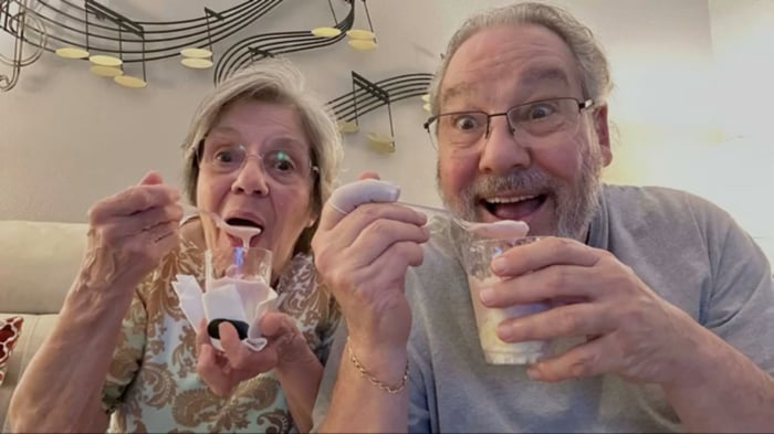 A photo of two people sitting on a couch eating cups of ice cream
