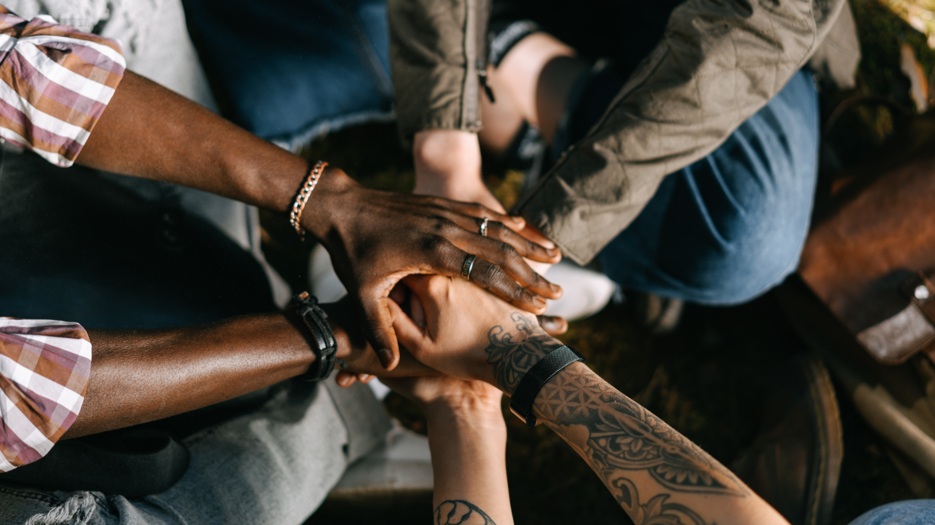 A diverse group of people stack their hands together in a circle, symbolizing teamwork, unity, and collaboration.