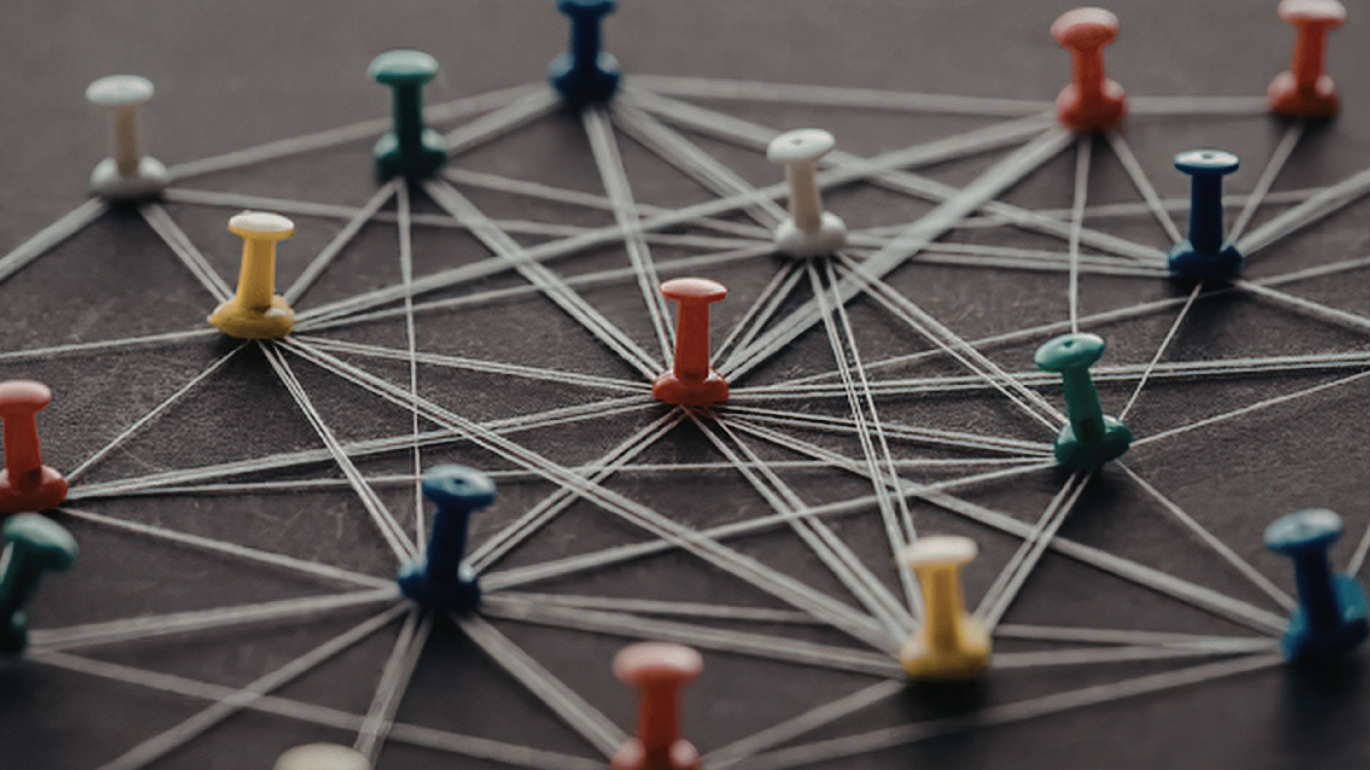 Colorful pushpins connected by white string form a web-like network on a dark surface.