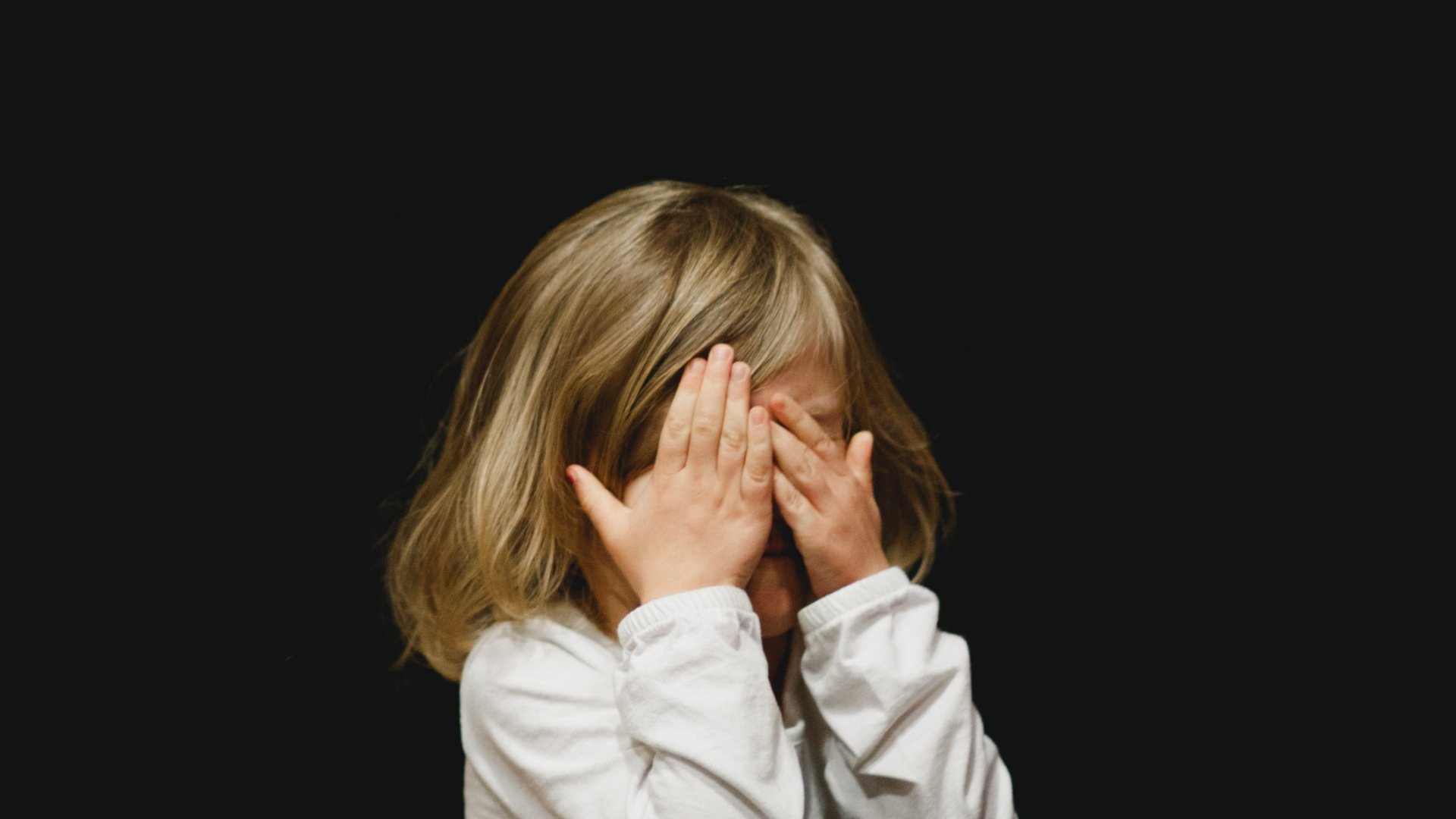 Child with face hidden behind their hands