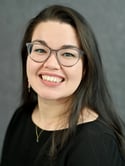 Woman with long straight brown hair wearing grey frame glasses smiles at the camera -Karyn Castro Headshot