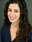 A woman with brown curly hair smiles at the camera - Kim Theodore Sidney Headshot 