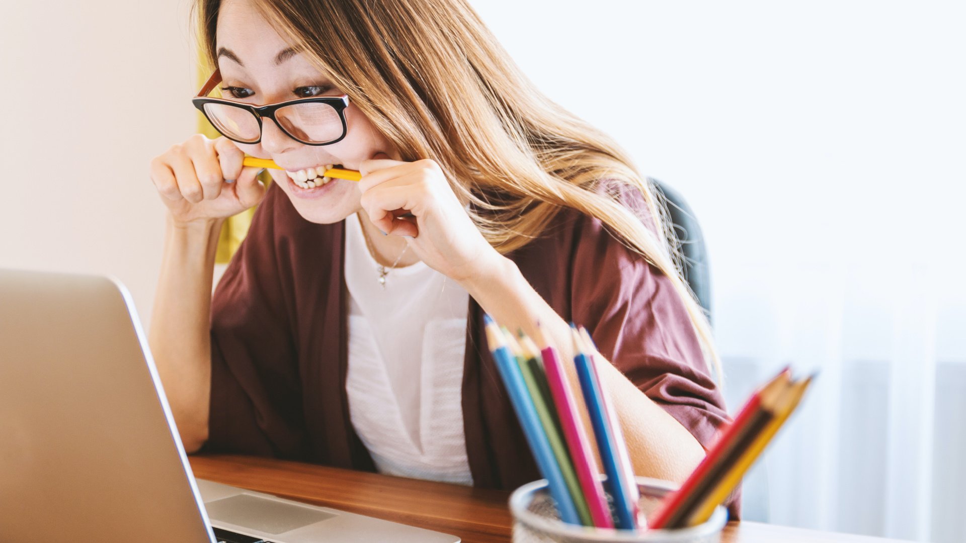 Woman sitting at desk with a laptop in frustration gripping a pencil in her teeth