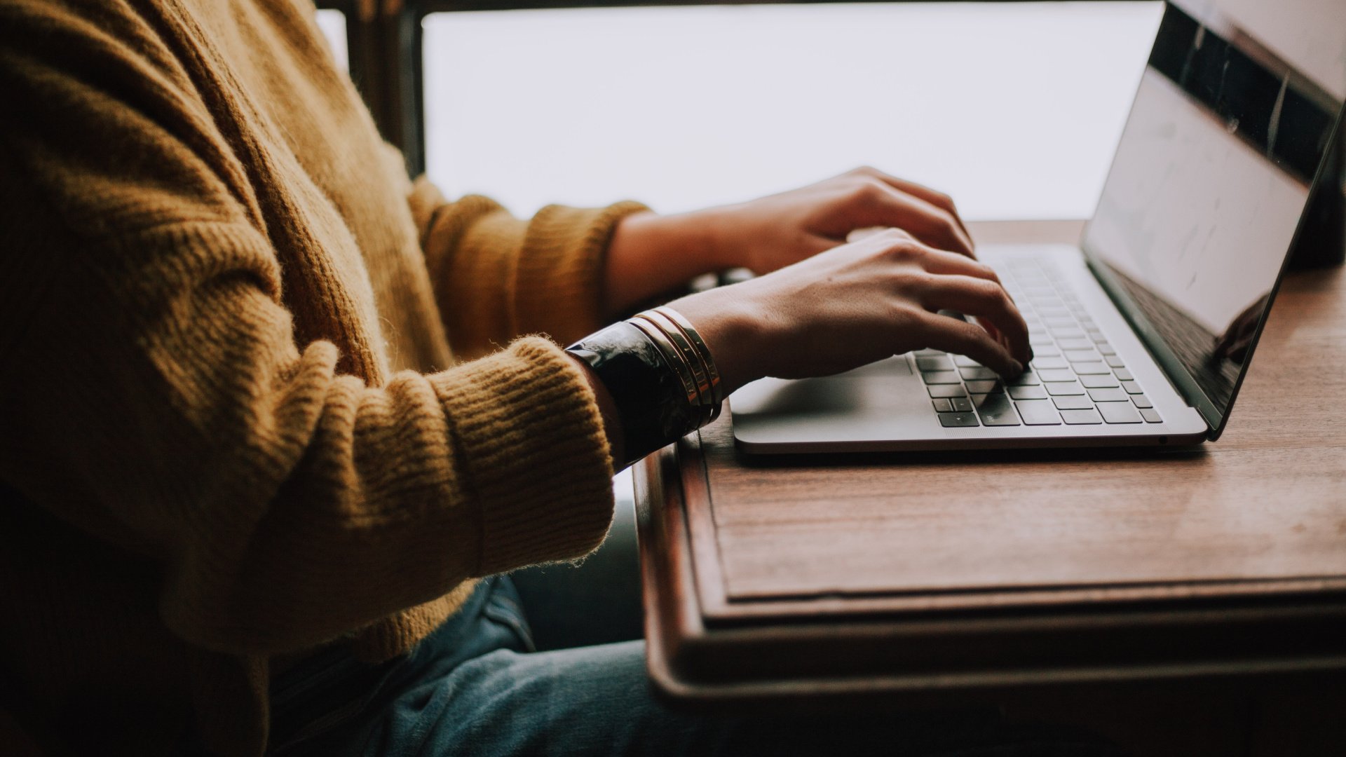 Person sitting at a desk with their hands on their laptop keyboard