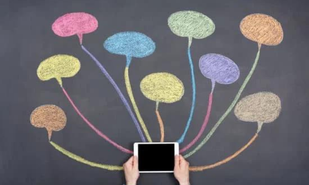Holding an iPad against a blackboard with conversation bubbles drawn in colored chalk