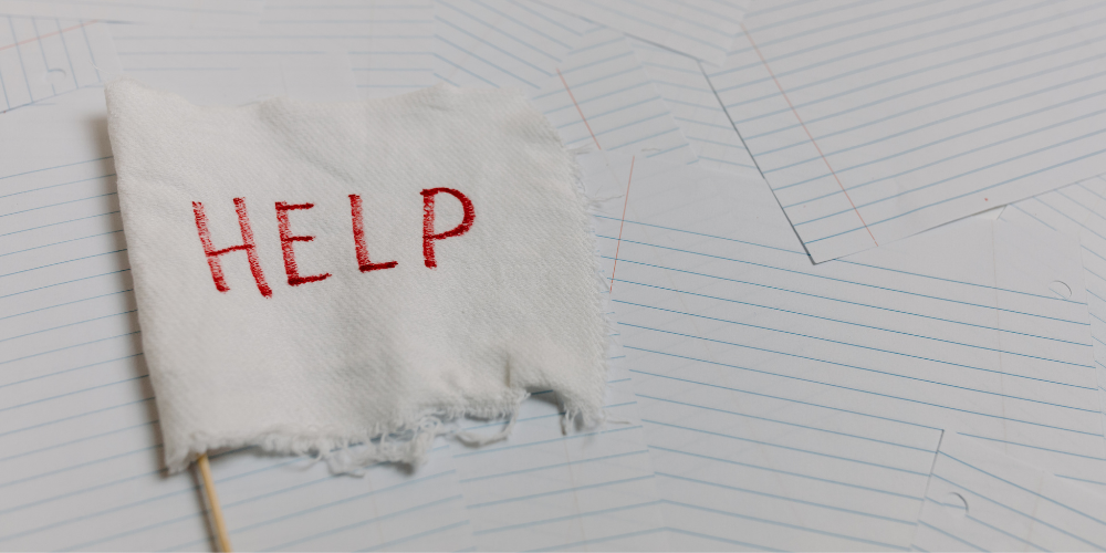 Homemade white flag with the word HELP on desk with papers