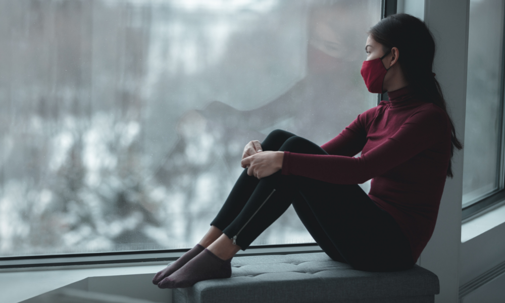 Masked woman with COVID anxiety looking outside through a window