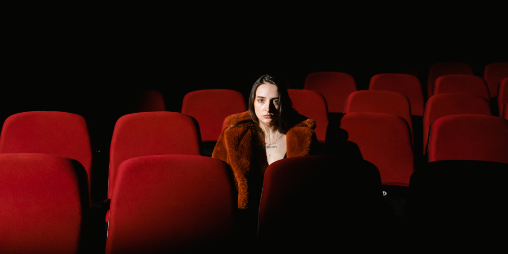 Woman seated in center of theater with red chairs