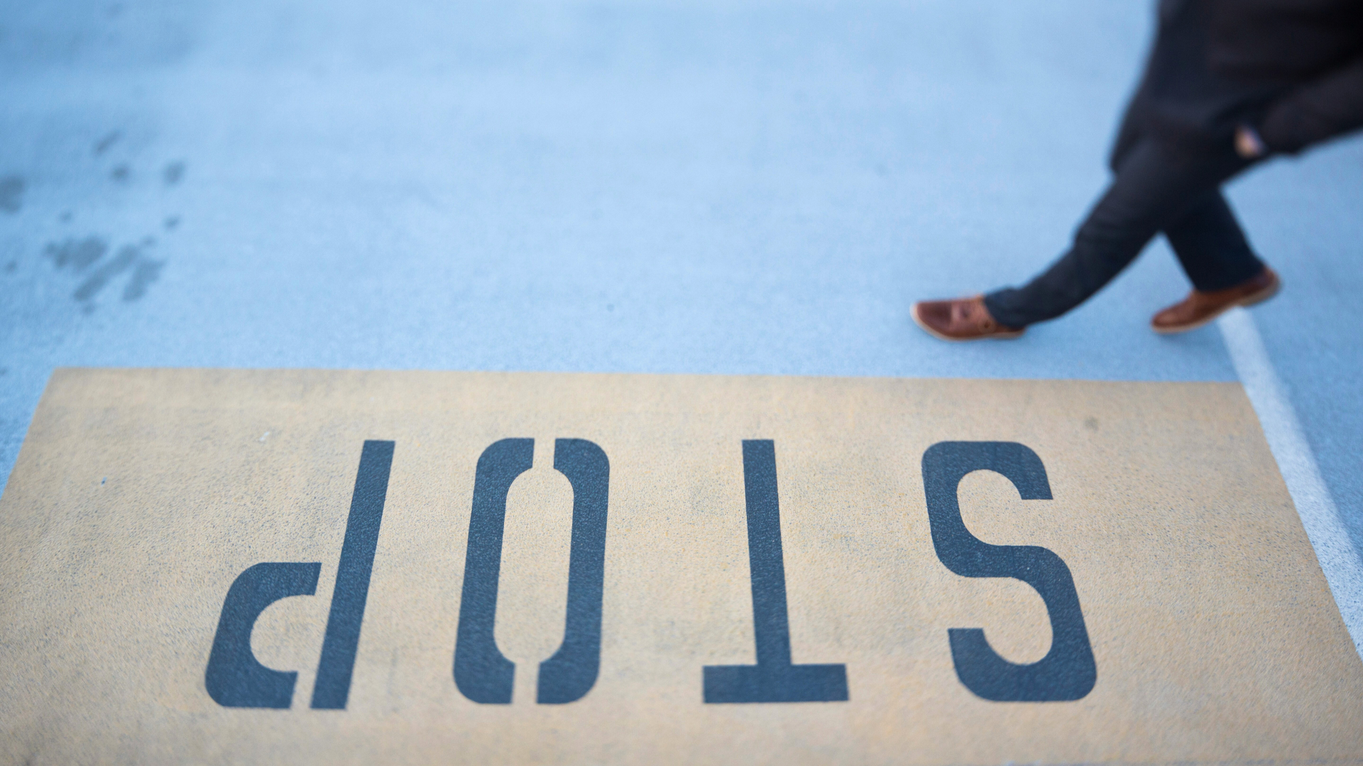 Person walking on gray pavement with the word _stop_ printed on the ground