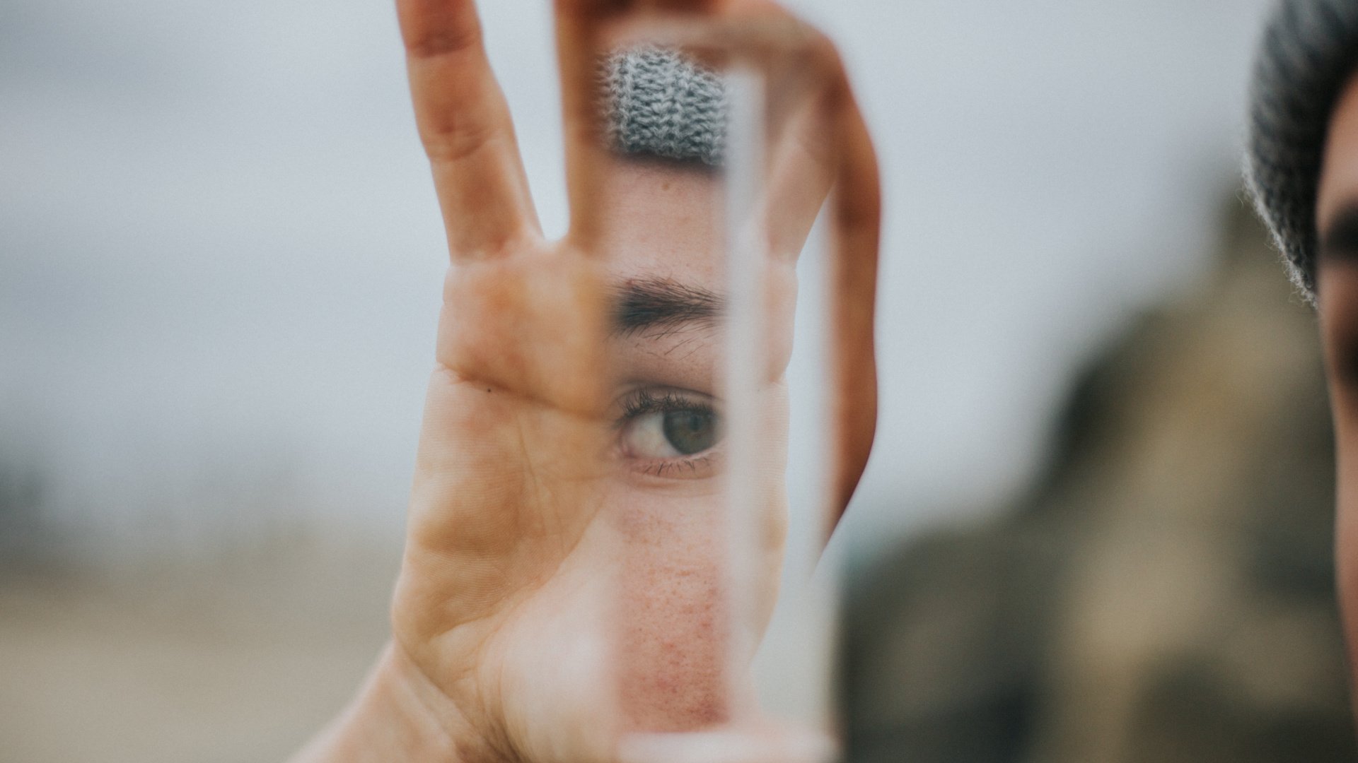 A hand holding a mirror reflecting the person's hand and eye 