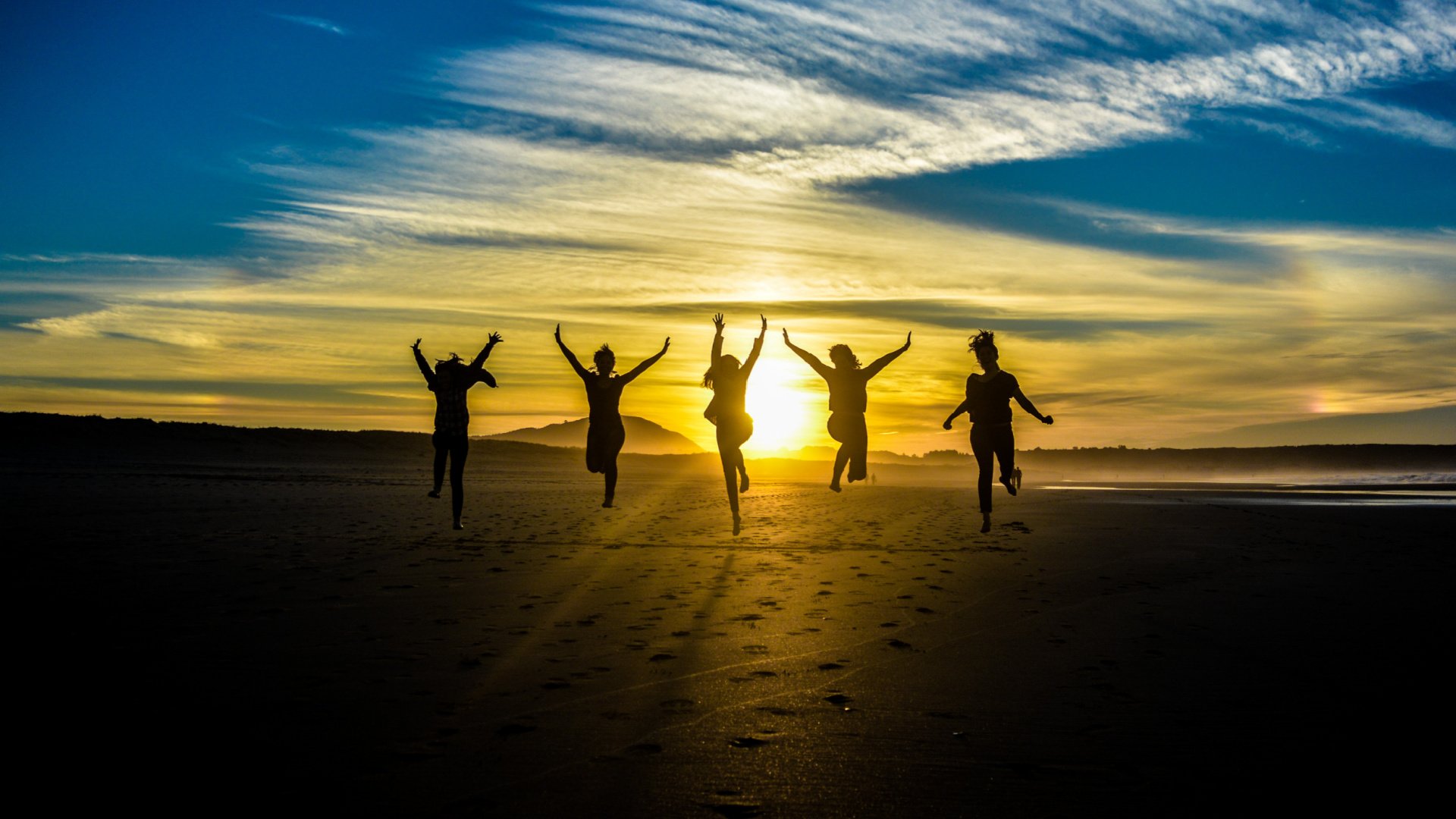 Five silhouettes jumping together into the air at sunset