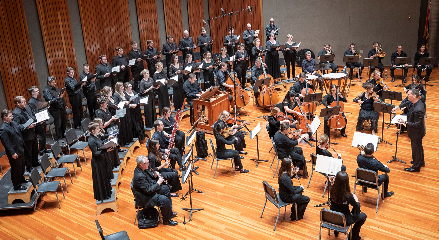 An aerial view of a choir and orchestra performing together on a large stage.