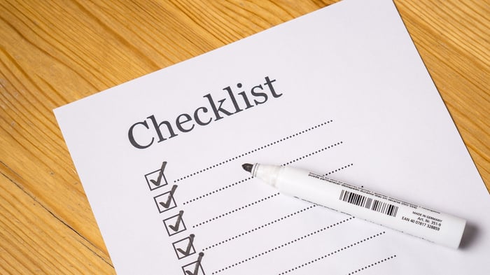 blank checklist on white paper on wooden surface with black marker resting on top