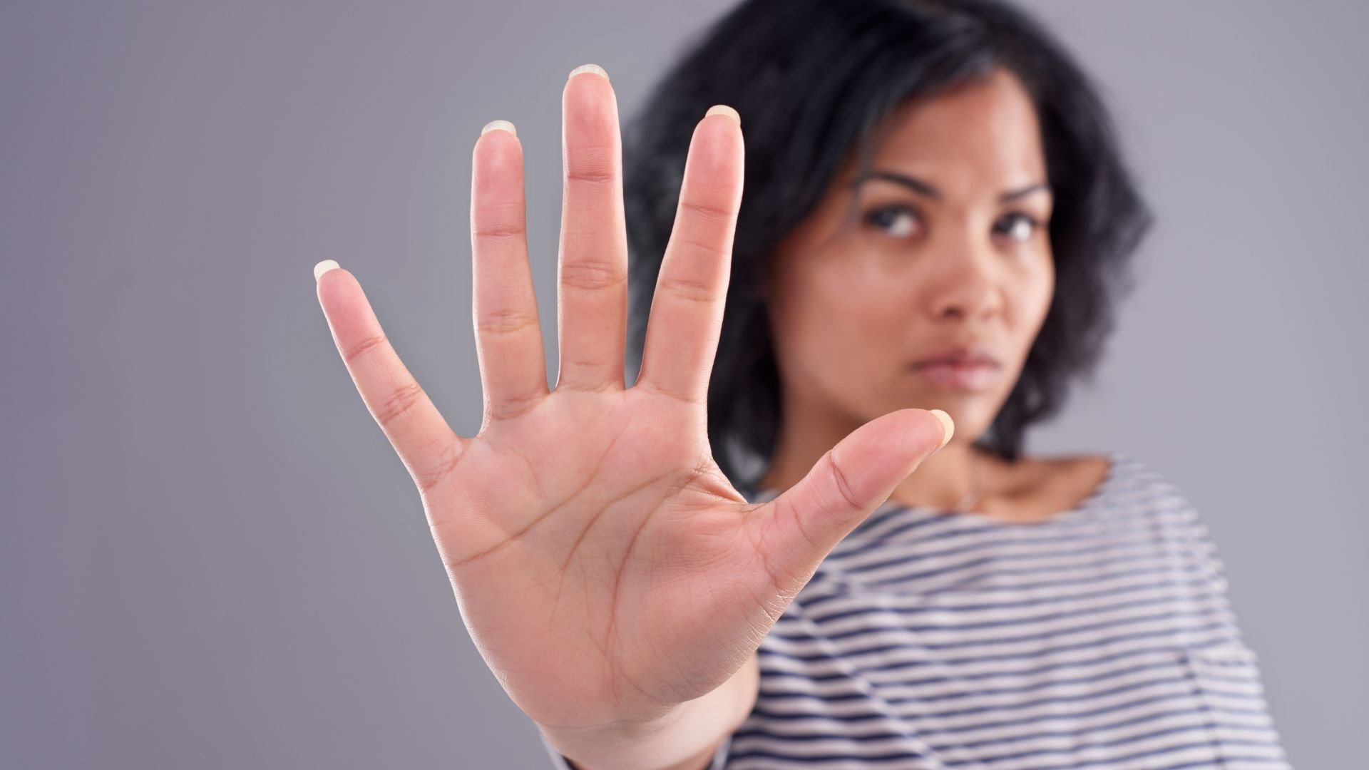 serious female in striped shirt holding out her hand palm out  indicating stop