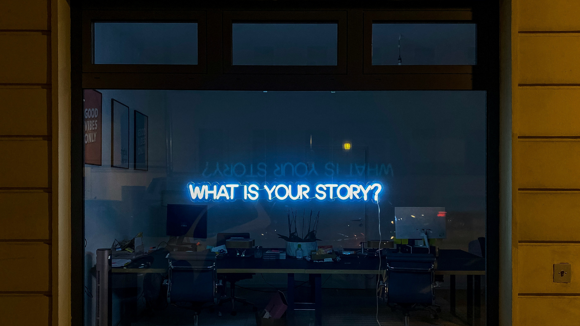 dark storefront window at night with a glowing neon sign in the words _what is your story