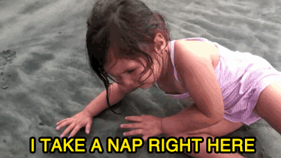 GIF of a dishevelled and soaked toddler on a beach in bathing suit laying on the wet sand. Text on the GIF reads, "I take a nap right here."