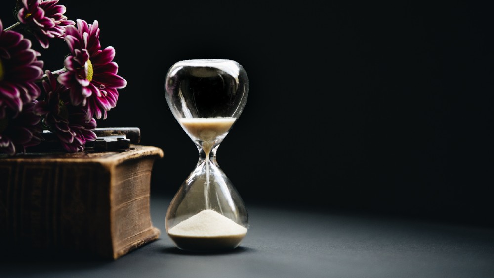 hourglass with sand next to purple floral arrangement