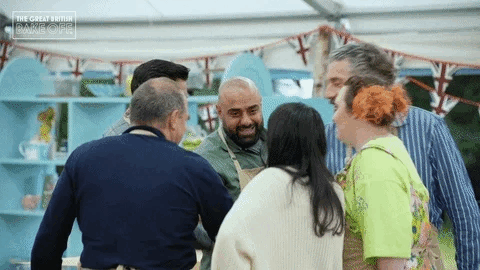 Group of baking show contestants raise their hands in a cheer before beginning their contest