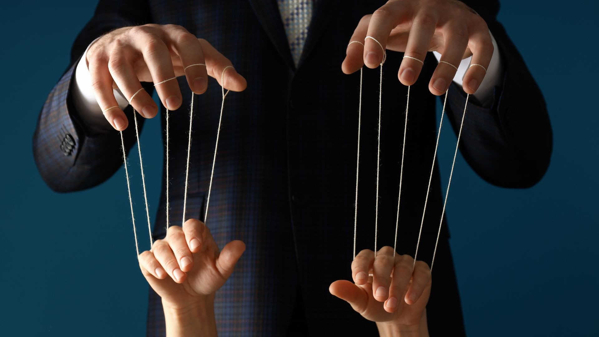 Person in a suit controlling two hands with puppet strings, symbolizing manipulation, control, or influence.