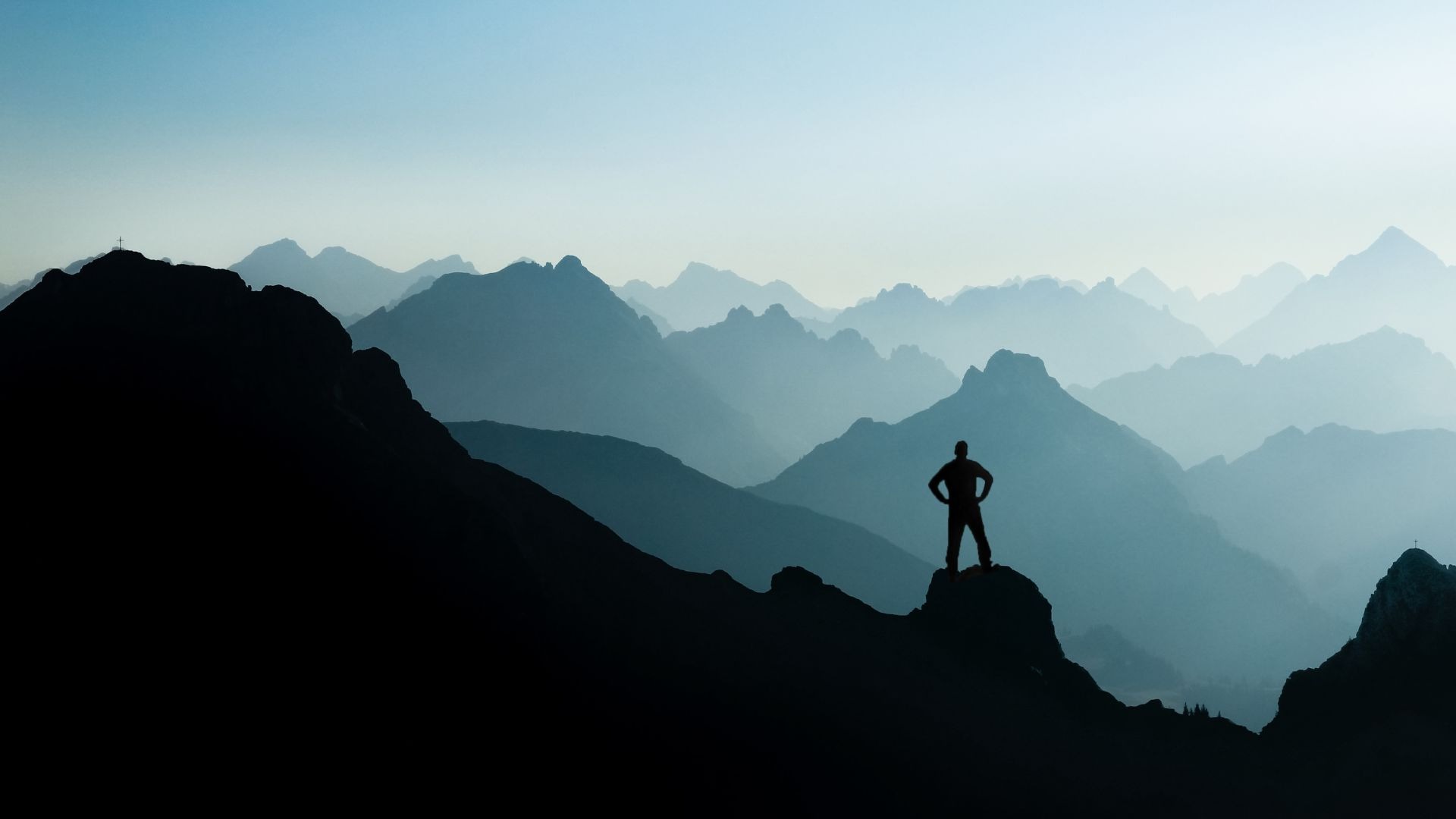 A silhouette of a person standing on a mountain peak as many more peaks gradually fade into the distance