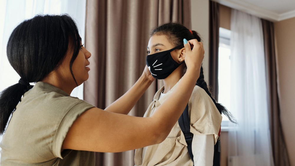 woman putting mask on child getting ready to go to school